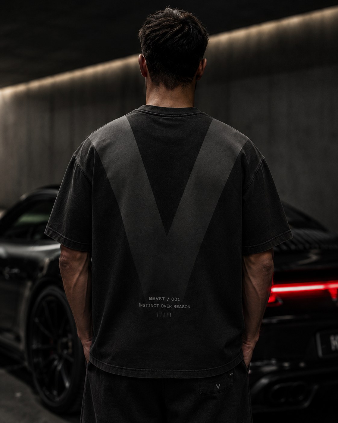 BEVST 001 tee worn at night beside a car, tail lights lit, the V visible from behind